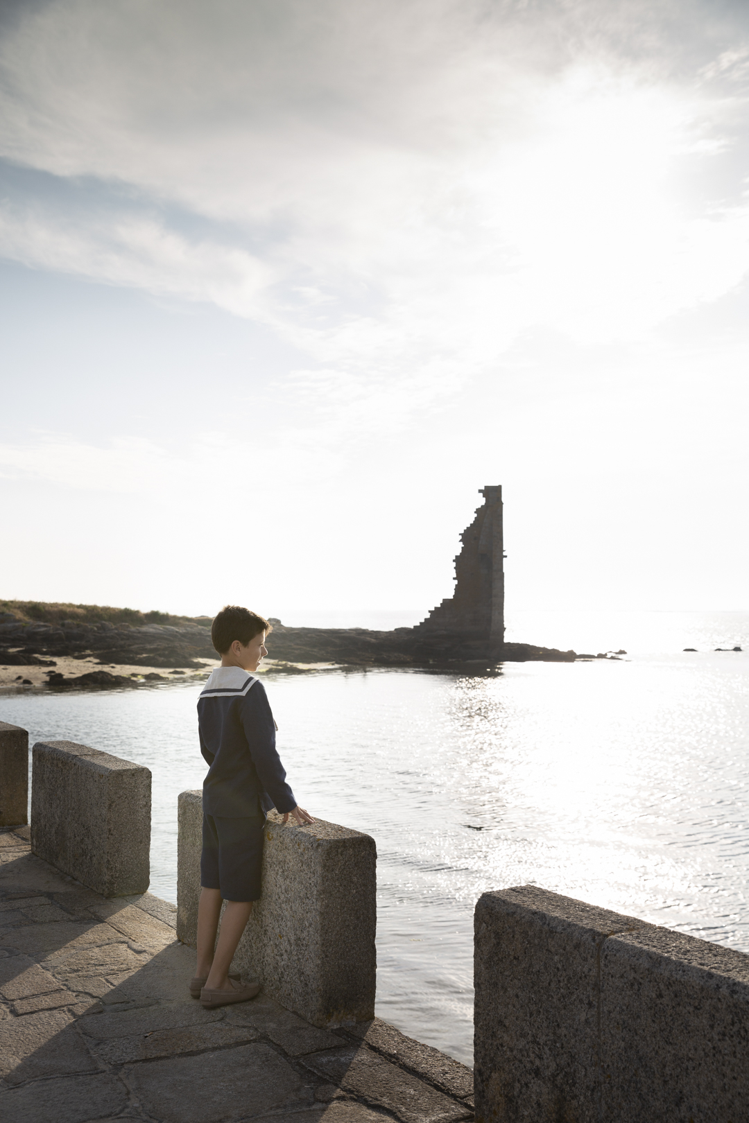 Niño de comunión observando un torreón junto al mar