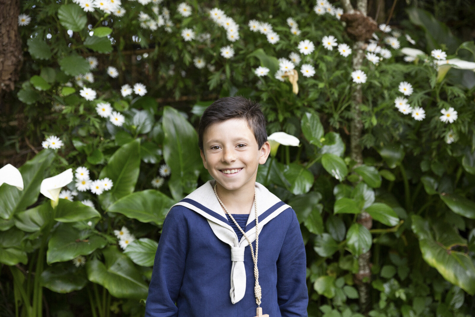 Niño de comunión entre arbustos con flores blancas