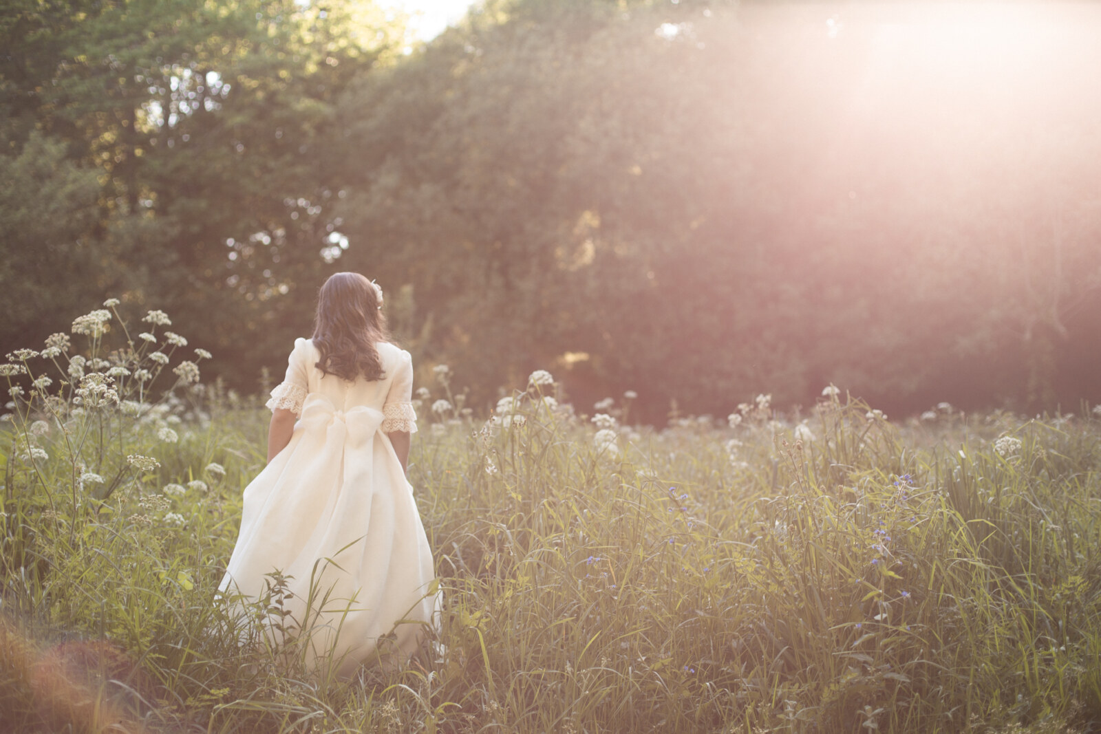 Niña de comunión caminando por un campo de flores silvestres