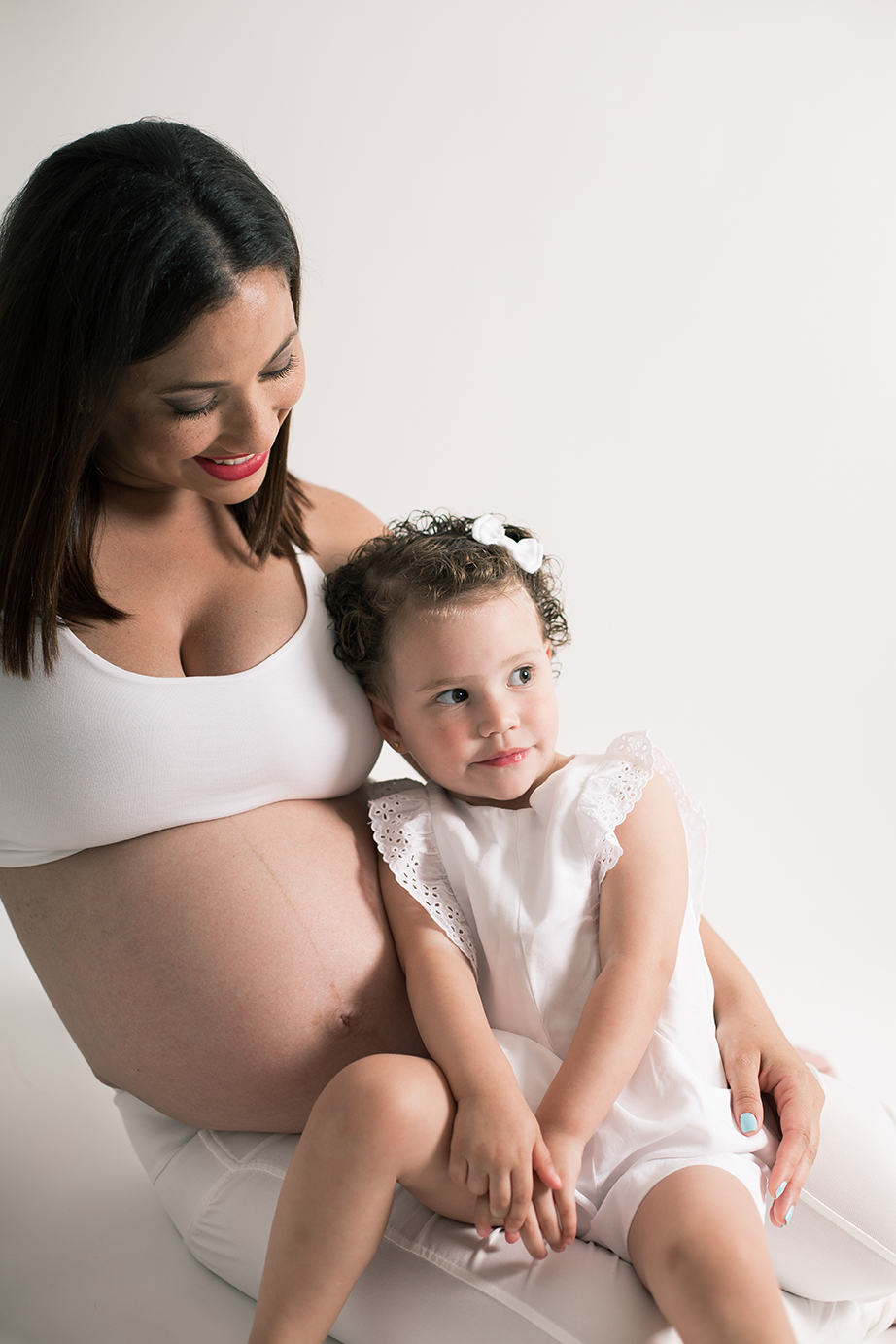 Madre embarazada con su hija en el regazo en sesión de maternidad en estudio