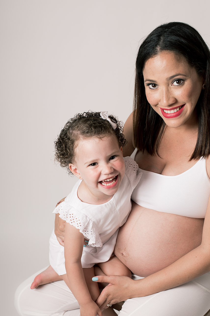 Madre embarazada y su hija sonriendo en sesión de maternidad en estudio