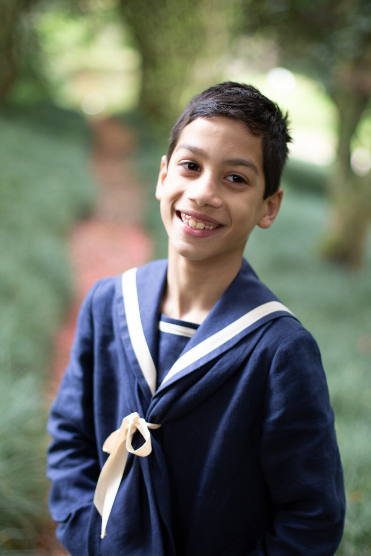 Niño con traje marinero azul sonriendo en un jardín, fotografía de comunión