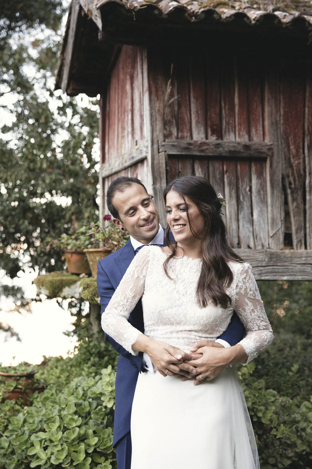 Novios abrazados y sonrientes en un jardín de piedra