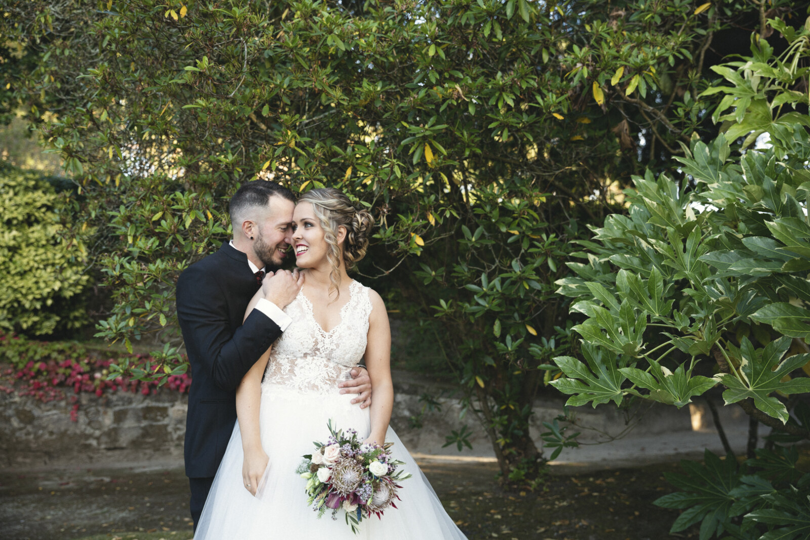 Novio besando la cabeza de la novia entre la vegetación de un jardín