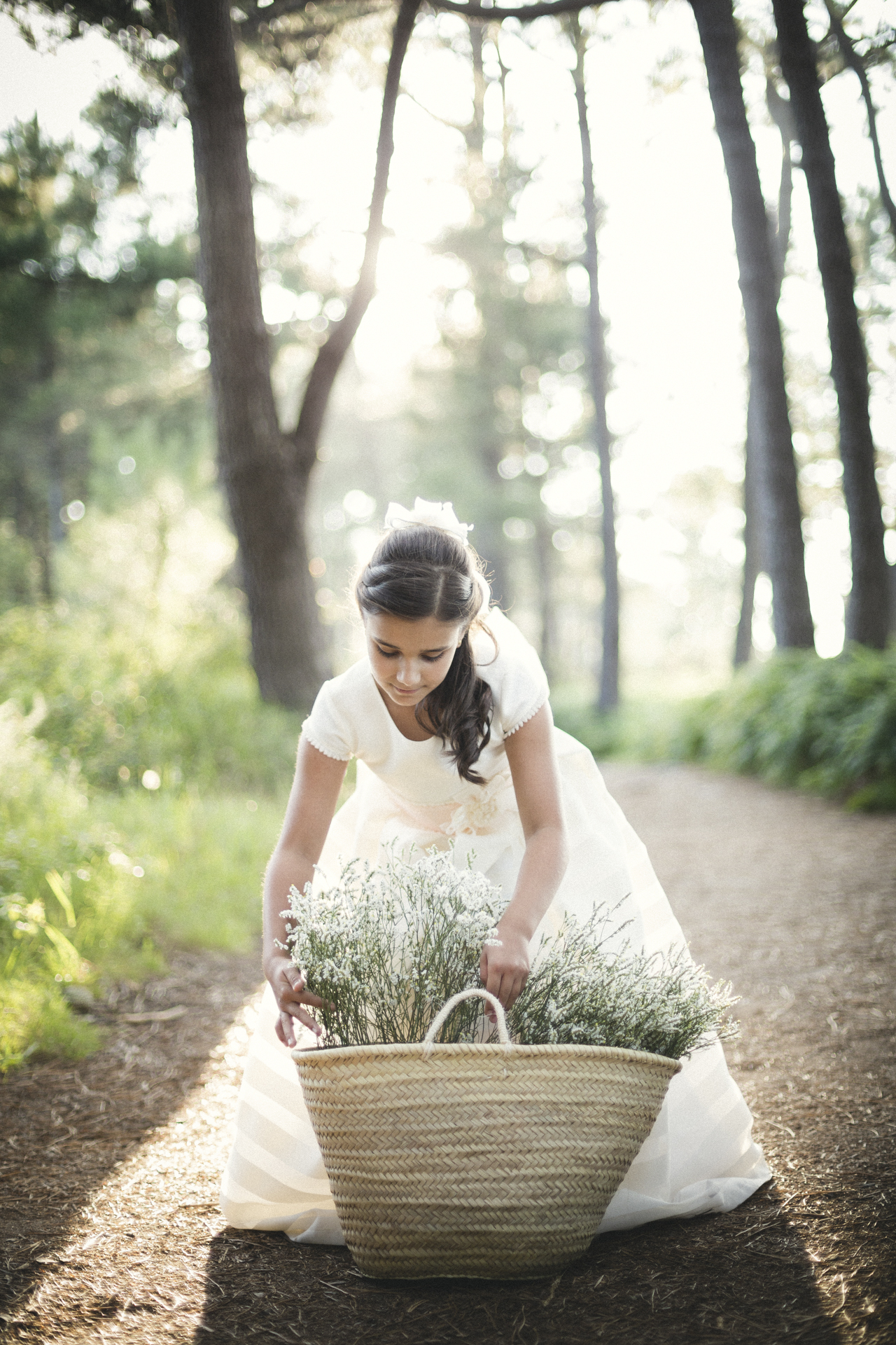 Niña de comunión cogiendo flores de una cesta en el bosque