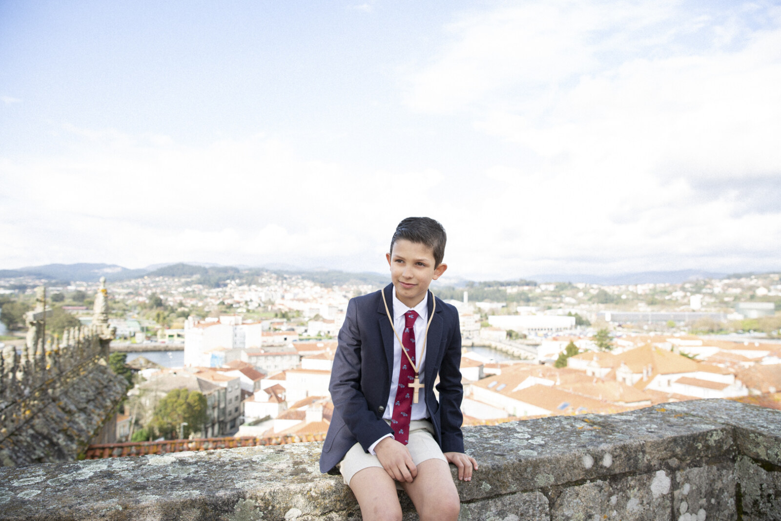 Niño de comunión sentado en una muralla con vistas a la ciudad
