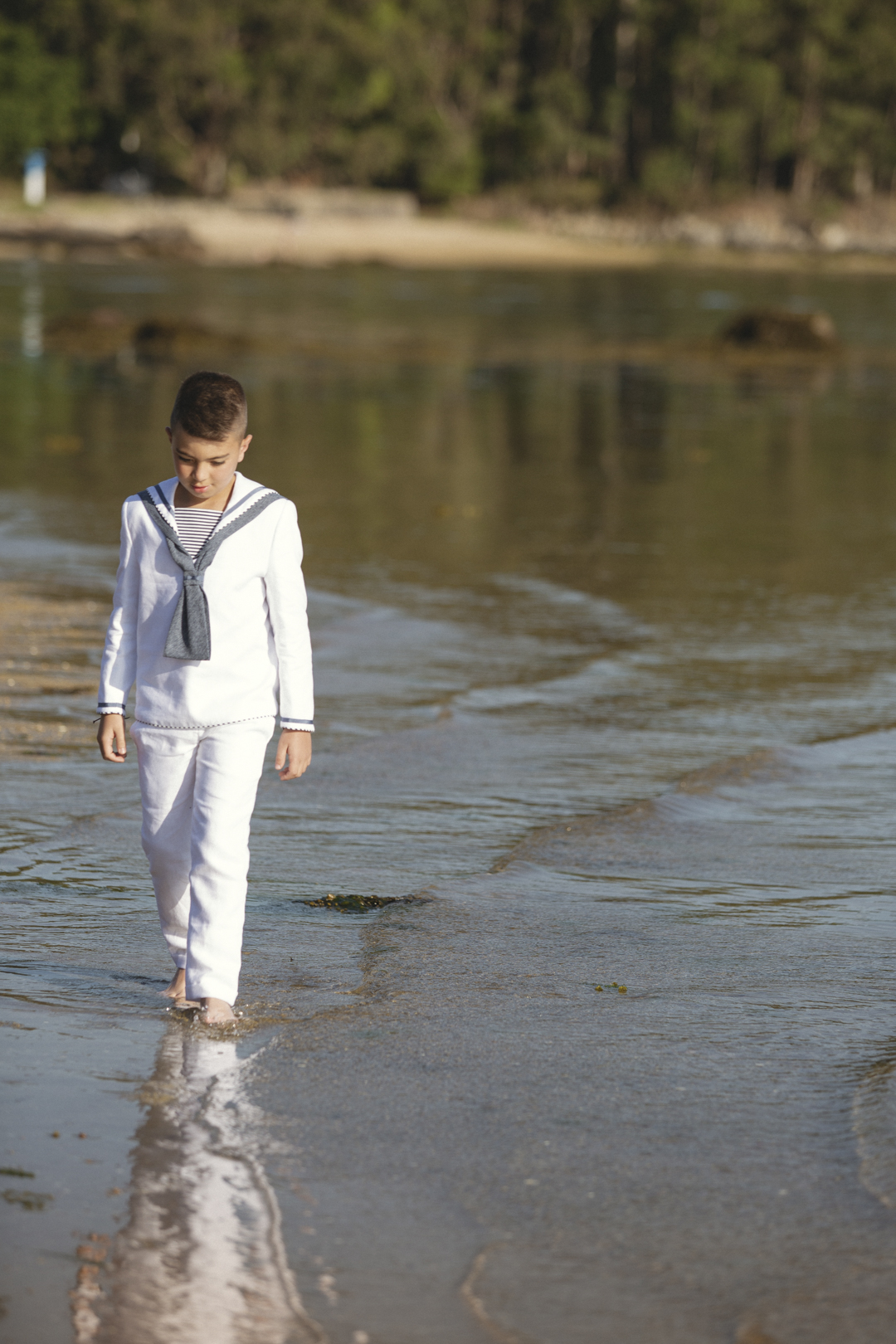 Niño de comunión caminando descalzo por la orilla del mar