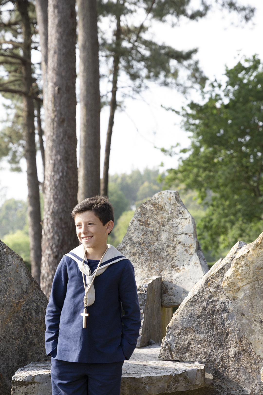 Niño de comunión junto a una gran roca en el bosque