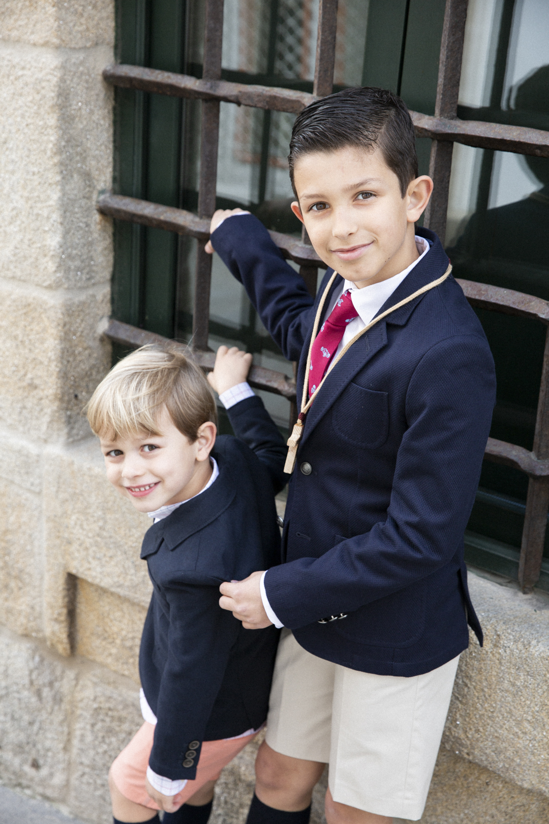 Dos niños de comunión, uno ajustando la chaqueta del otro