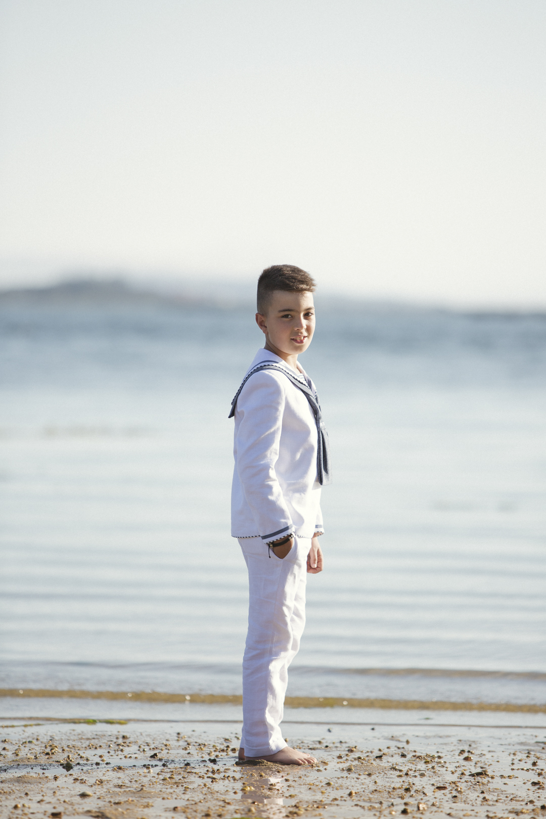Niño con traje marinero de pie en la orilla de la playa