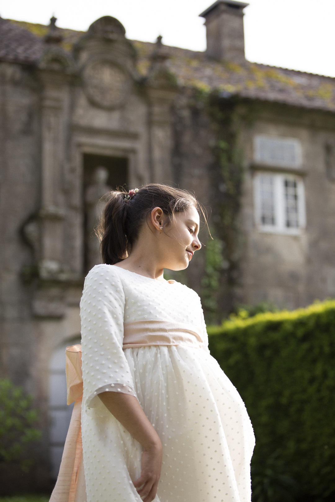 Niña de comunión con vestido de corte imperio frente a un pazo