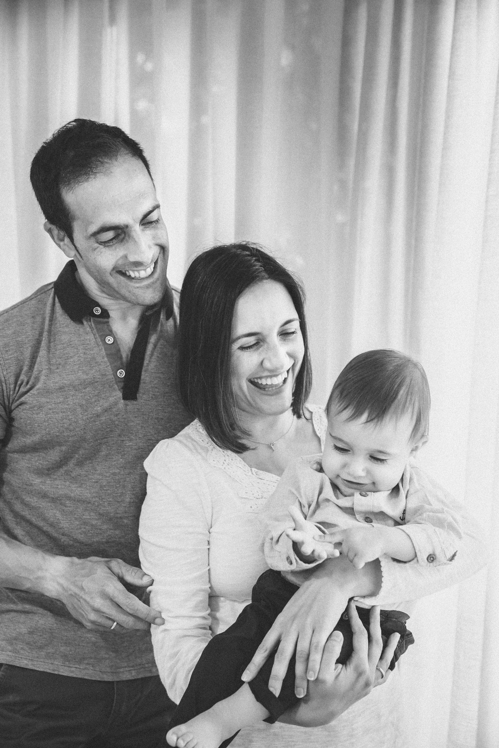 Padre, madre y bebé riendo juntos en una sesión de familia en blanco y negro