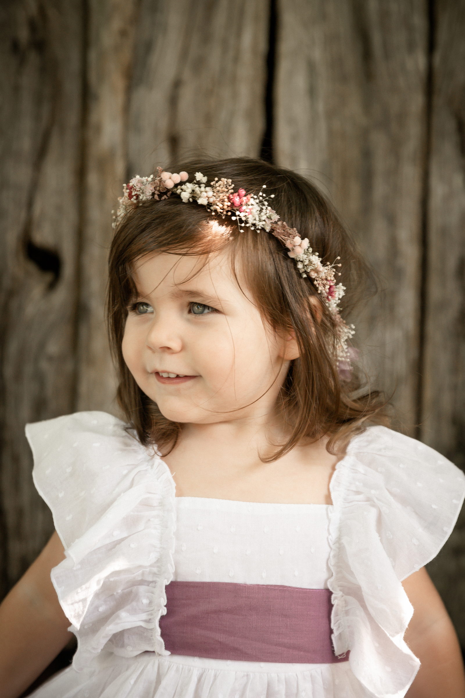 Niña con corona de flores de perfil junto a un muro de madera