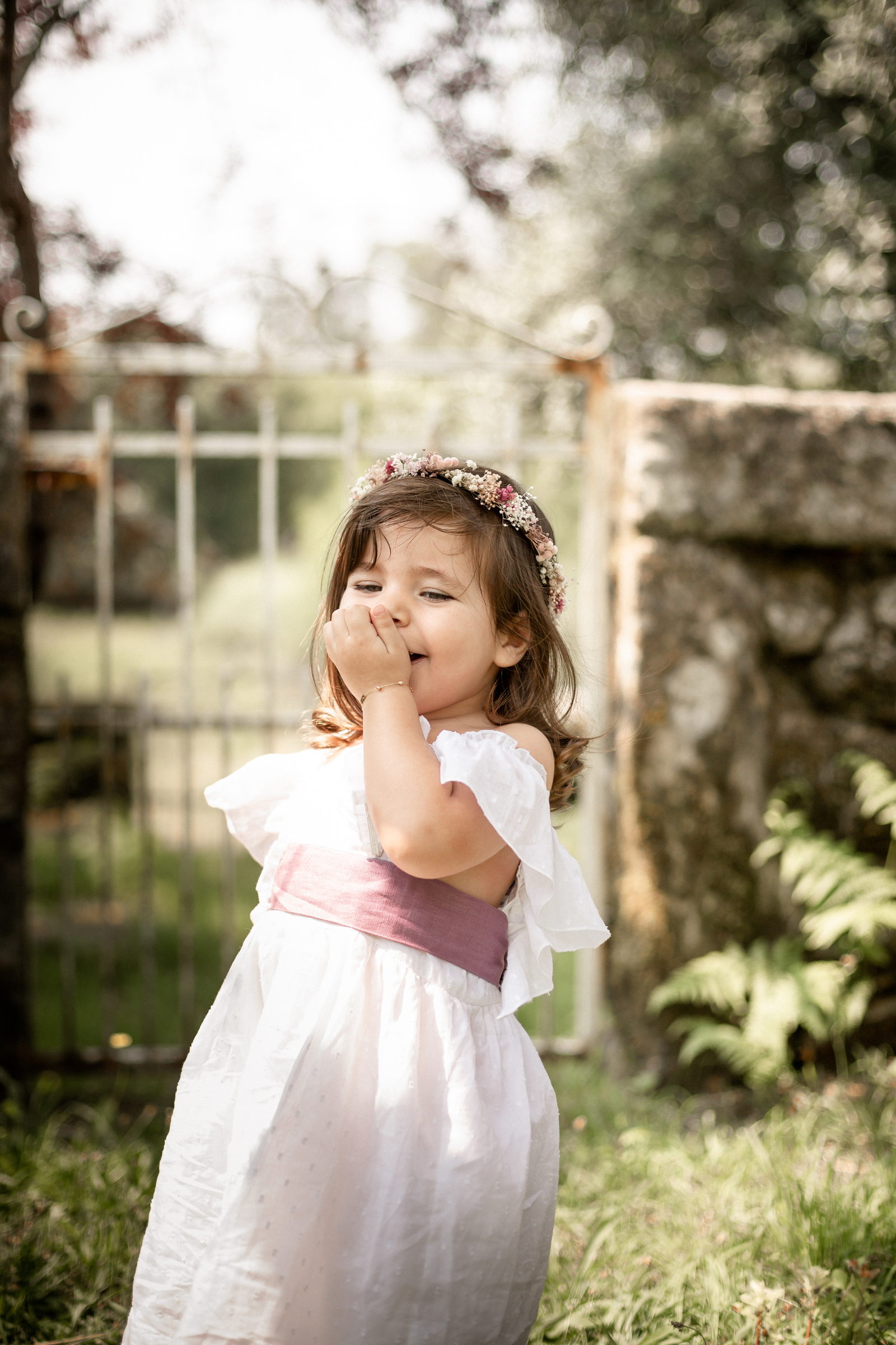 Niña con vestido blanco y lazo rosa caminando por el jardín