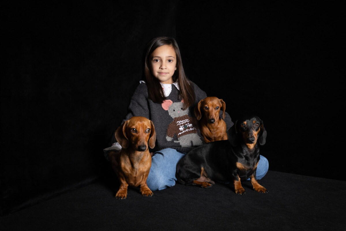 Tres perros teckel posando junto a su dueña sobre fondo negro