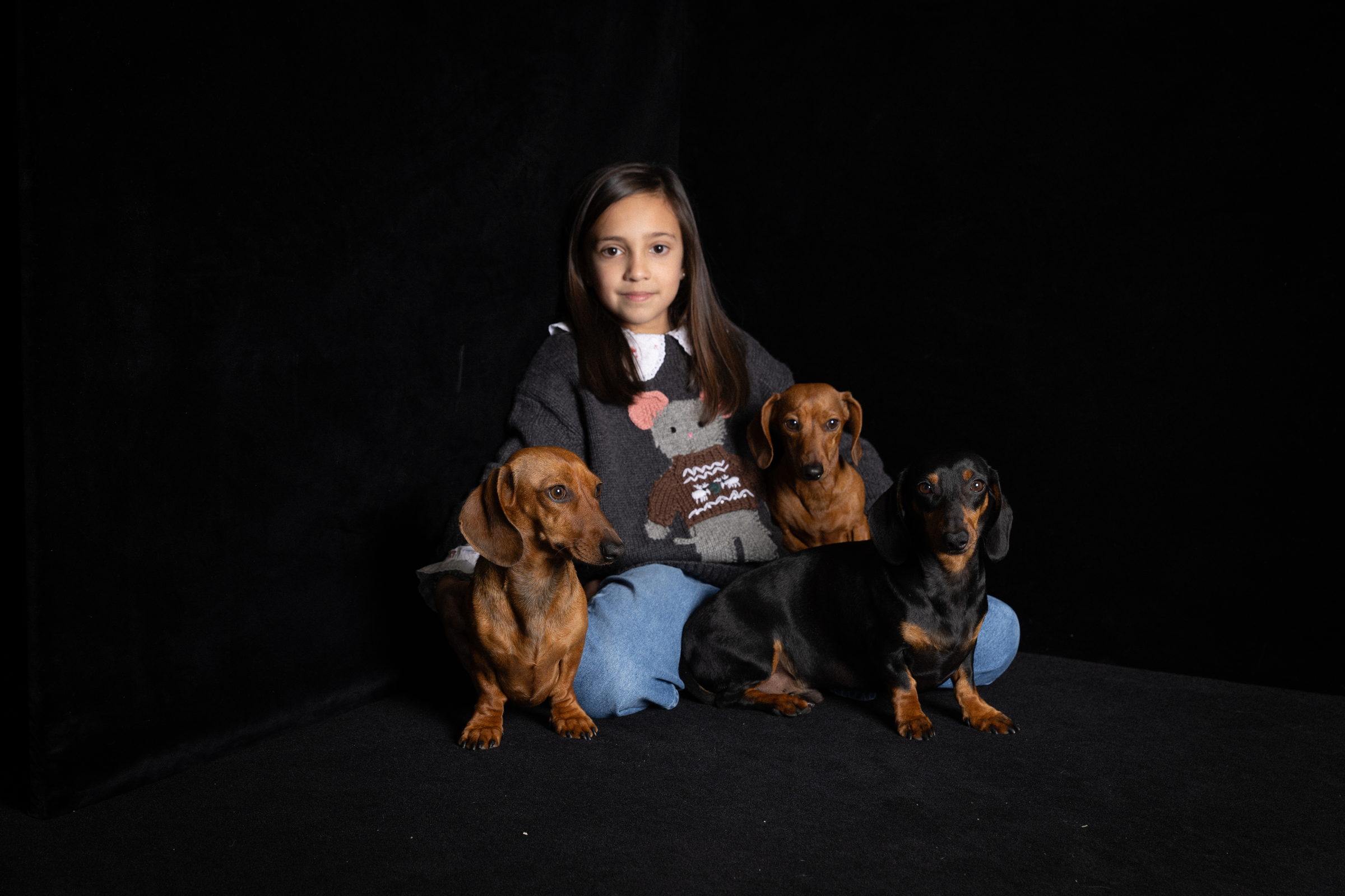 Niña sentada en el suelo del estudio con sus tres perros teckel