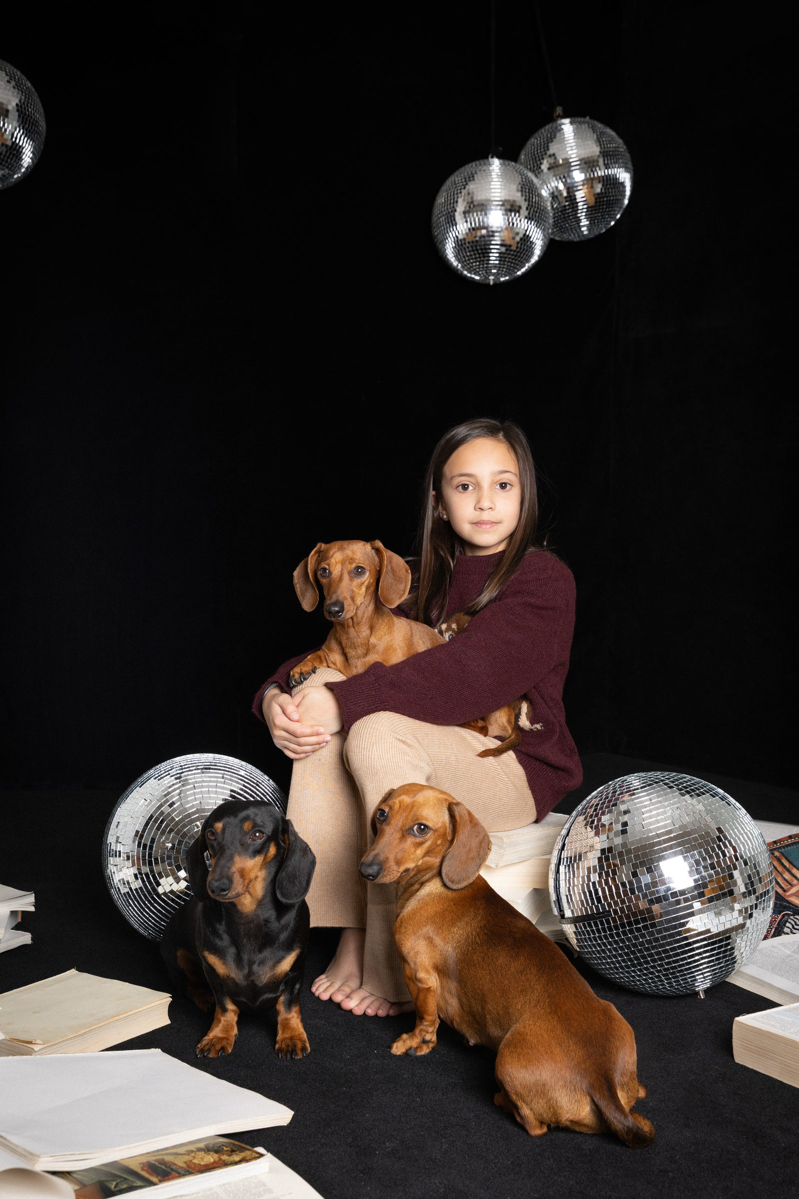 Niña abrazando a sus perros teckel en un estudio con bolas de espejo