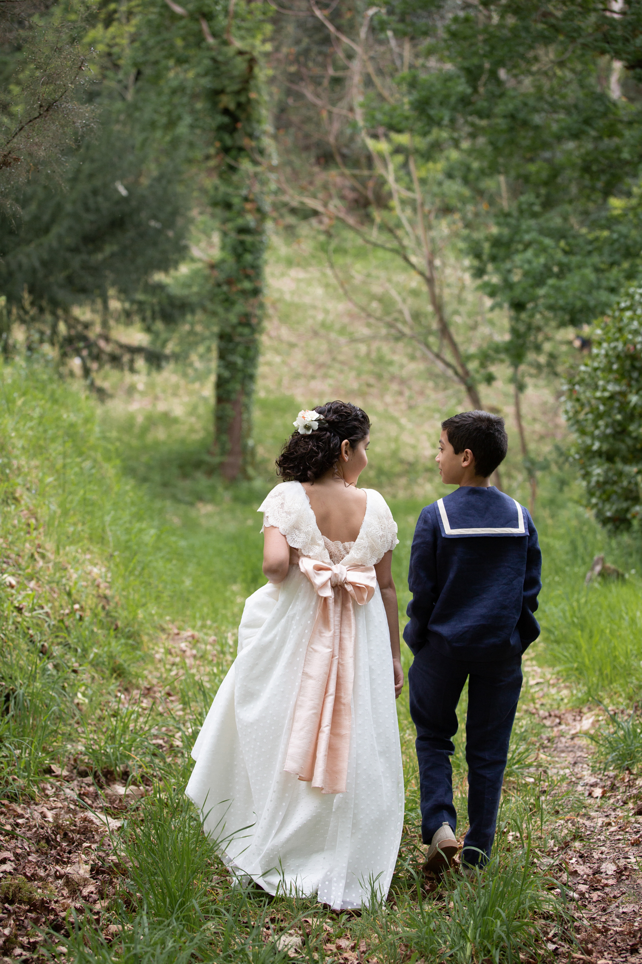 Hermanos caminando de la mano por un bosque el día de la comunión
