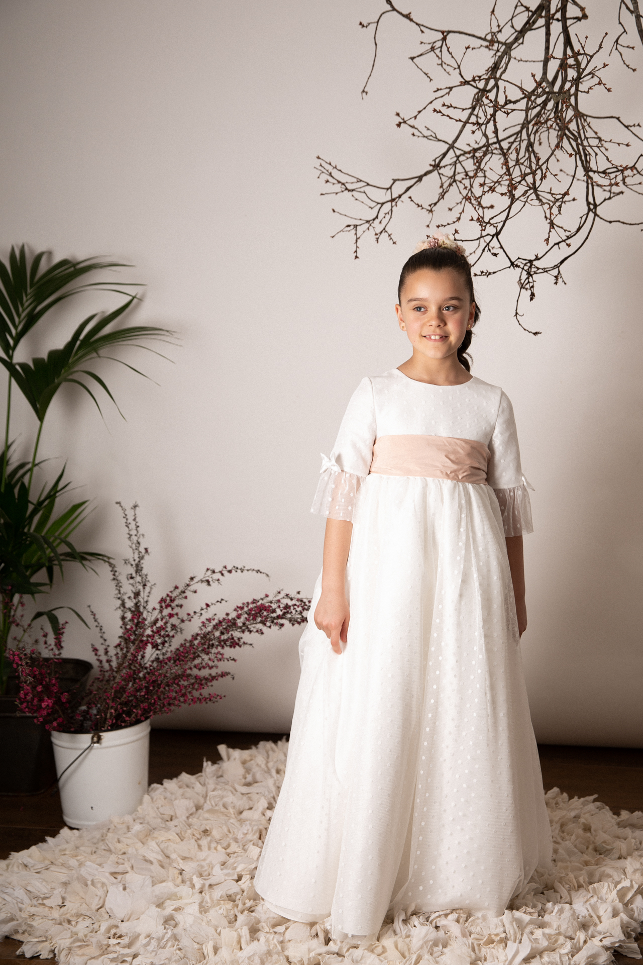 Niña de comunión sentada entre pétalos de flores en estudio