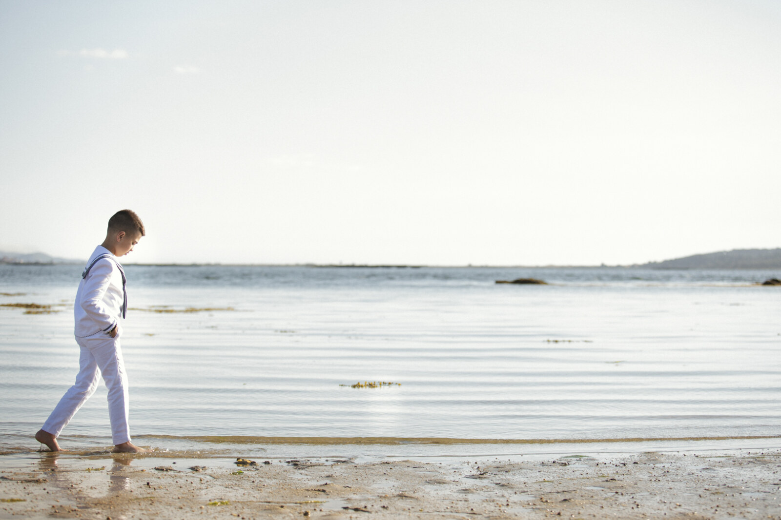 Niño de comunión caminando por una playa amplia
