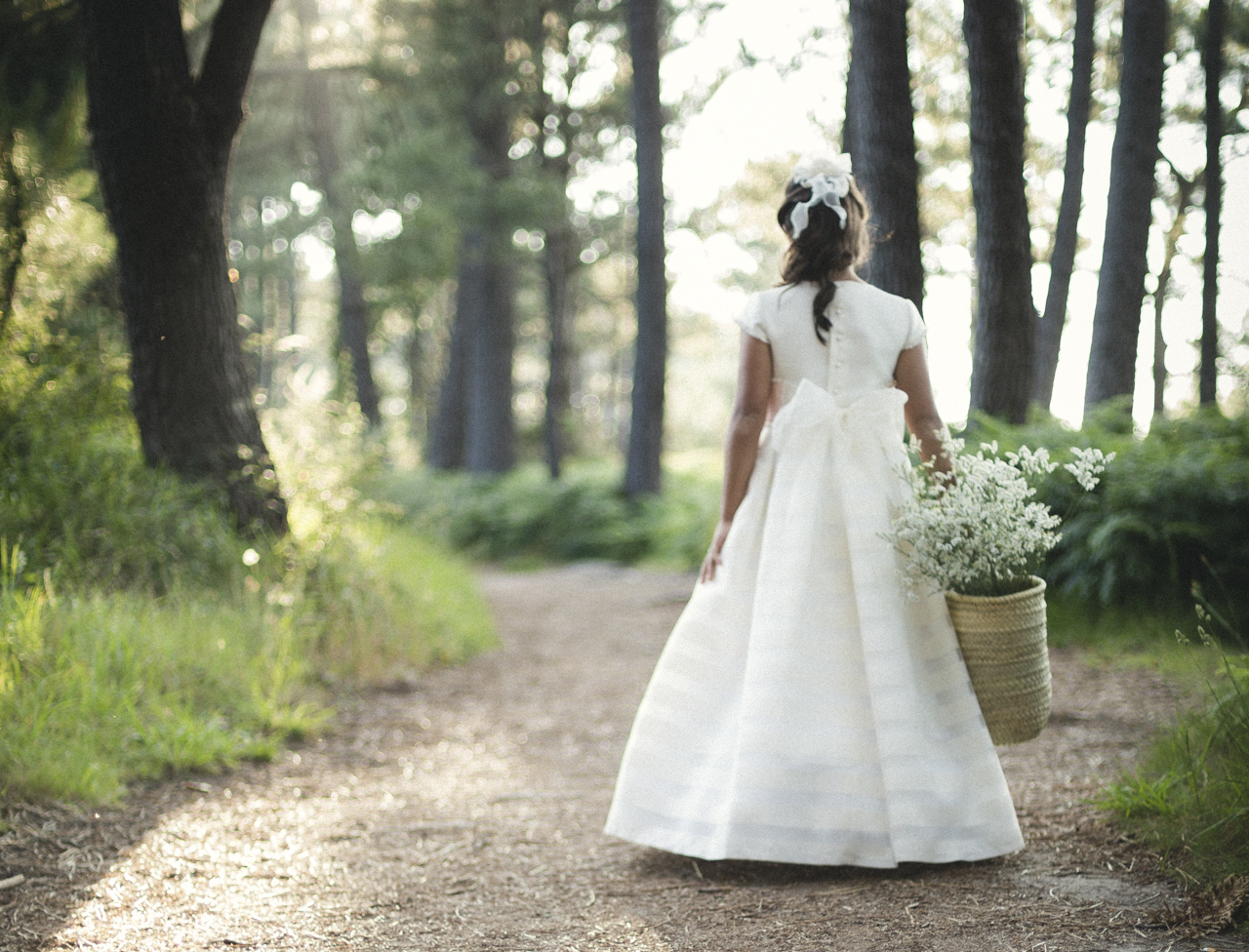 Niña de comunión con cesta de flores en el bosque