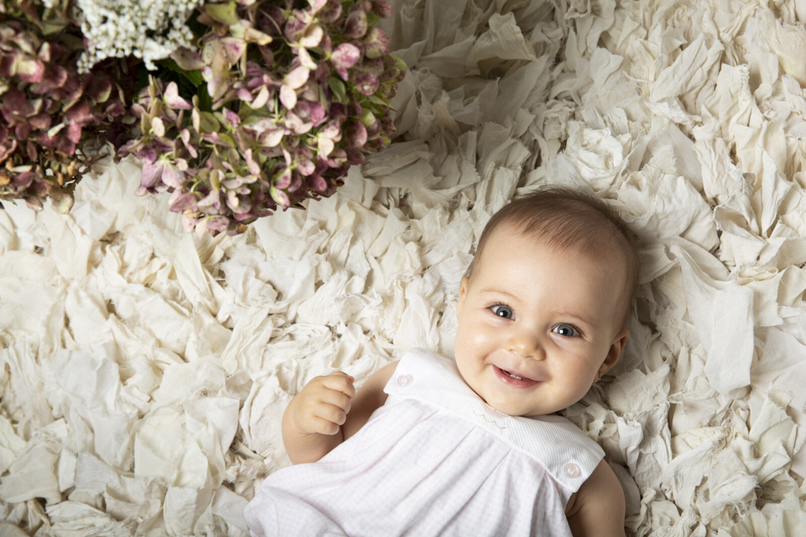 Bebé sonriente en sesión de estudio con flores secas