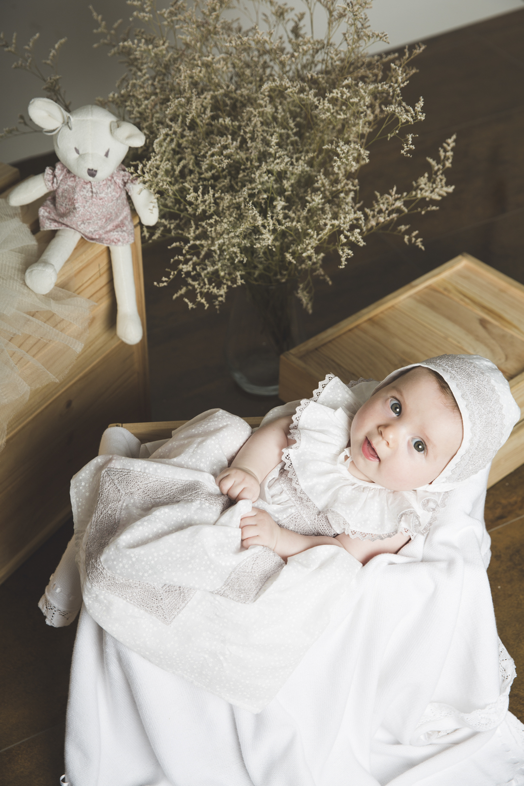 Bebé con gorrito recostado junto a un peluche en estudio