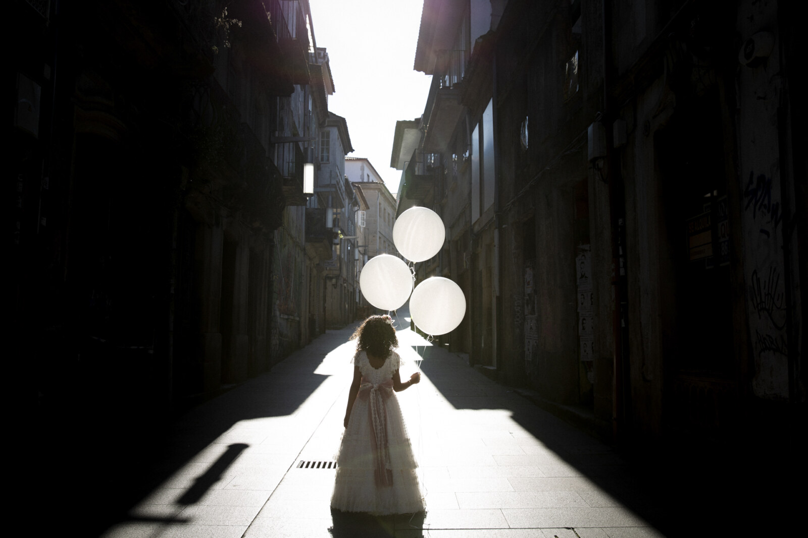 Globos blancos flotando en una calle del casco antiguo, día de comunión