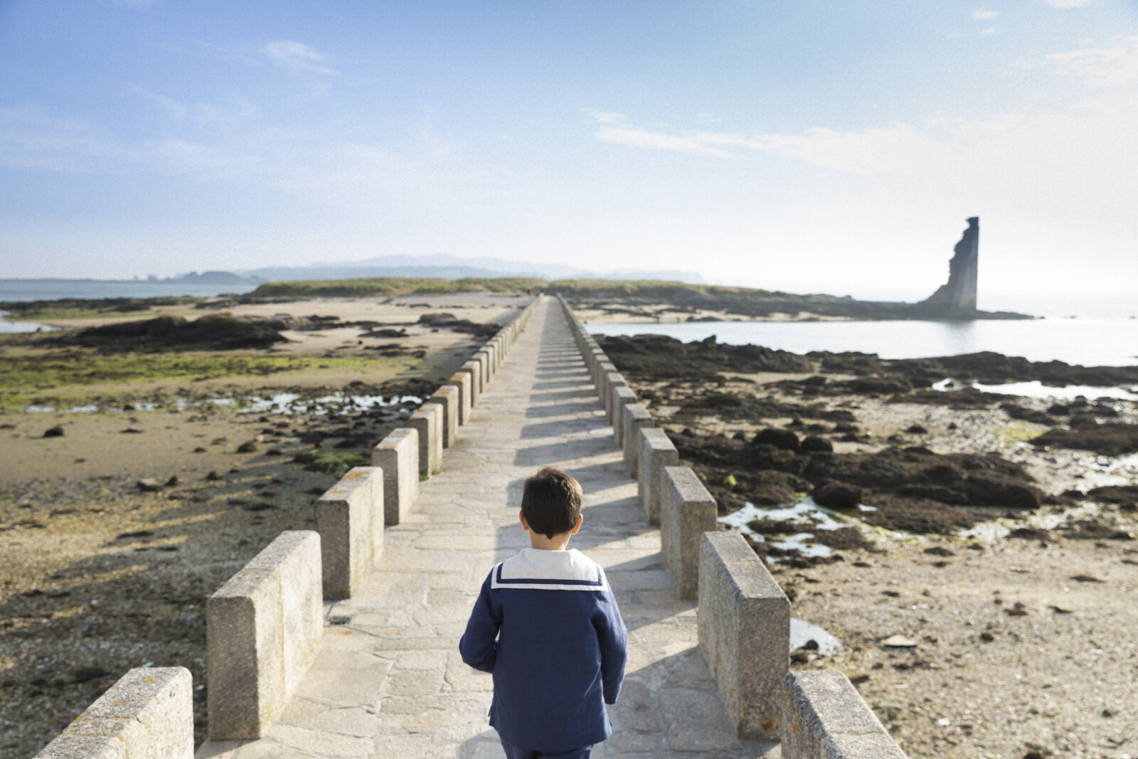 Niño de comunión caminando por un paseo marítimo hacia el faro en Sanxenxo