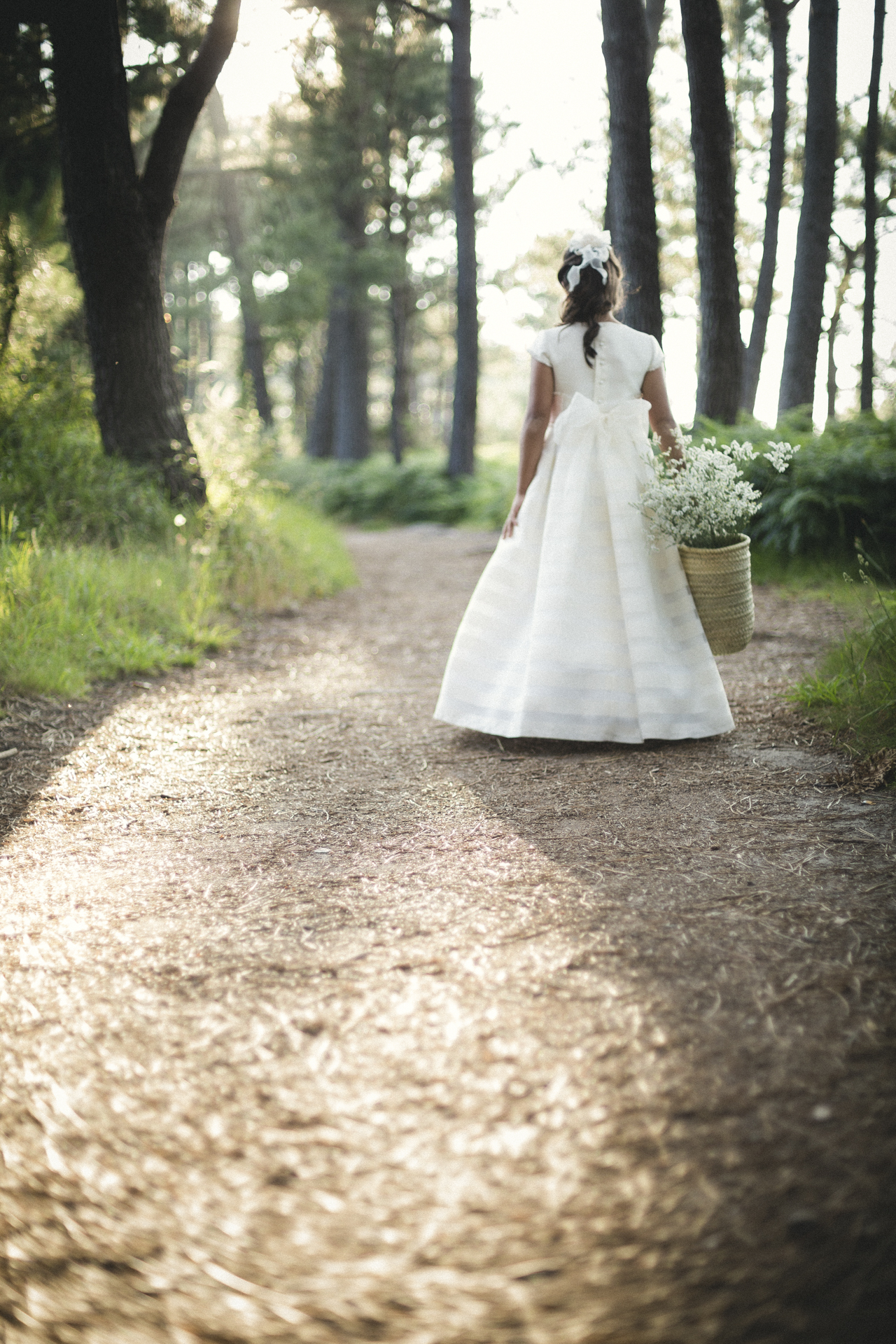 Niña de comunión caminando por un camino de grava a contraluz